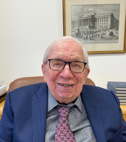 Prof. Tolley at his desk with a picture of the US Treasury where he worked behind him.