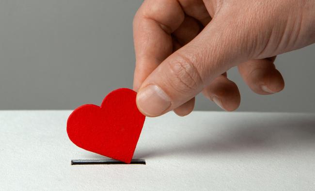 a hand donating a small heart as if it were a coin