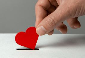 a hand donating a small heart as if it were a coin